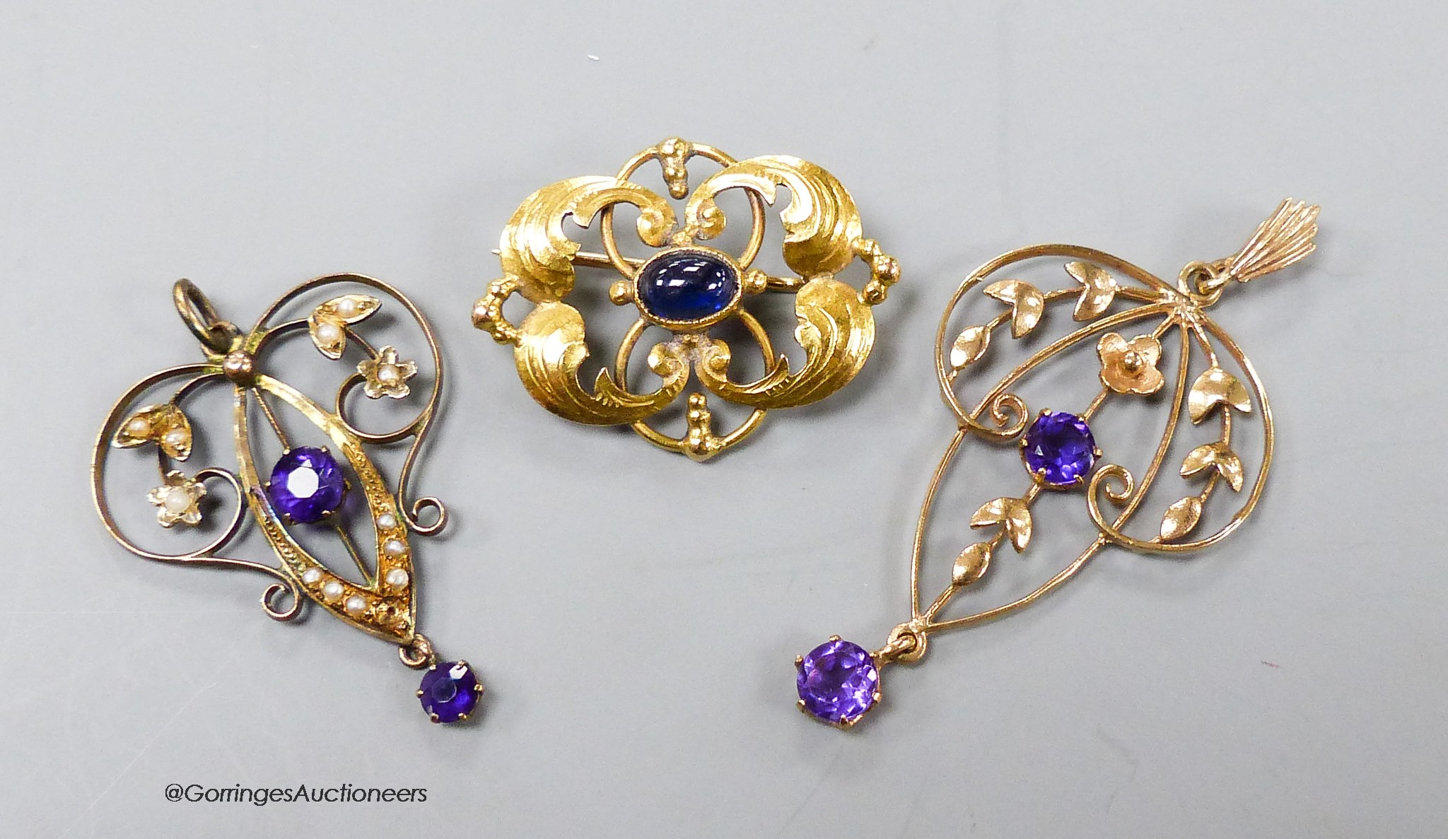 Two early 20th century yellow metal and amethyst set drop pendants, one stamped 9ct with seed pearls, largest 38mm, gross 3.7 grams and a 585 yellow metal and cabochon sapphire set brooch, gross 3.3 grams.